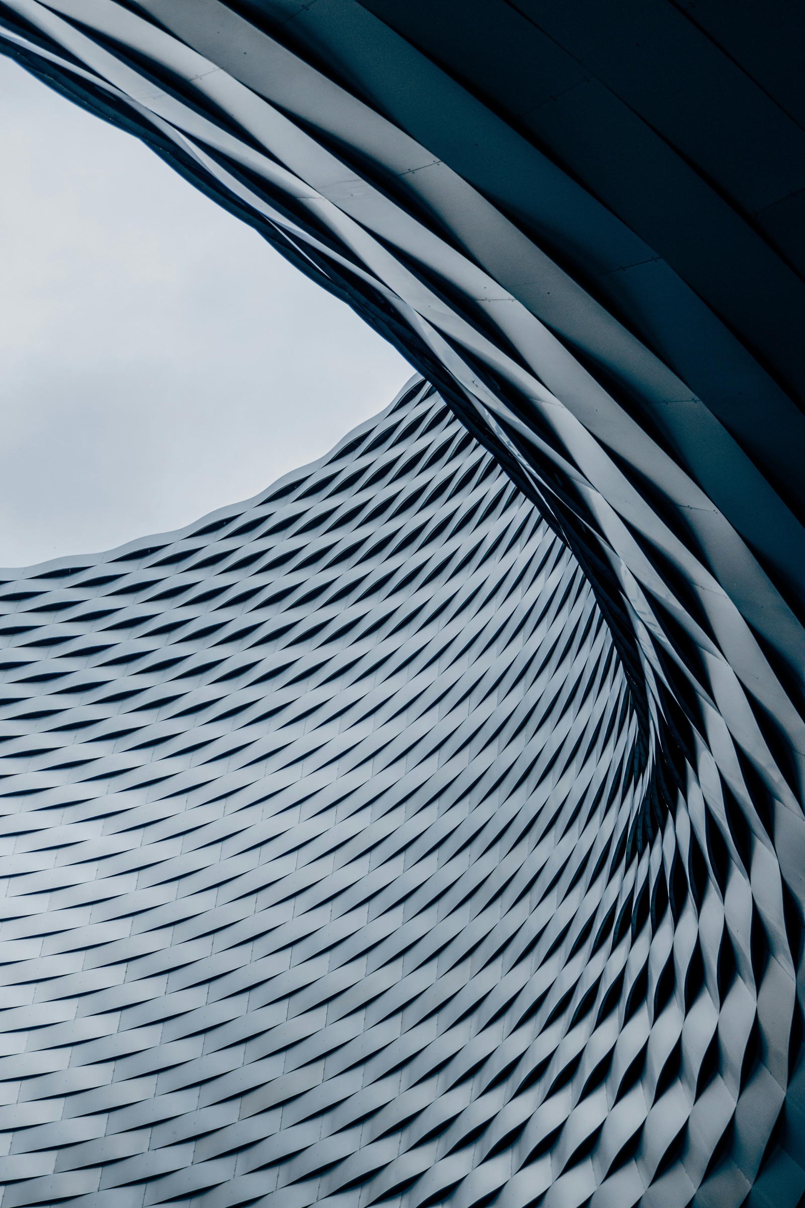 Detail of a woven stainless-steel facade curving overhead in cool blue-grey tones.